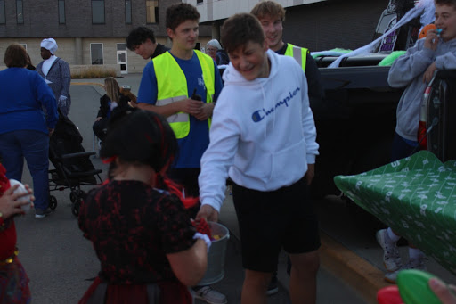 Sophomore Mike Anderson gives out candy to a young trunk-or-treater at the football trunk. The football team put up a game where kids got to throw toy footballs at targets to hit the players’ heads.