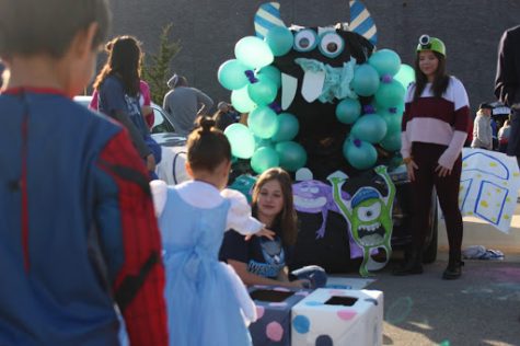 Freshman Andie Rau and sophomore Olivia Keiter watch as a young girl tosses a bean bag to win a prize at the Student Council trunk.