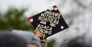 A graduated DREAMer holds their DACA-inspired hat up high.