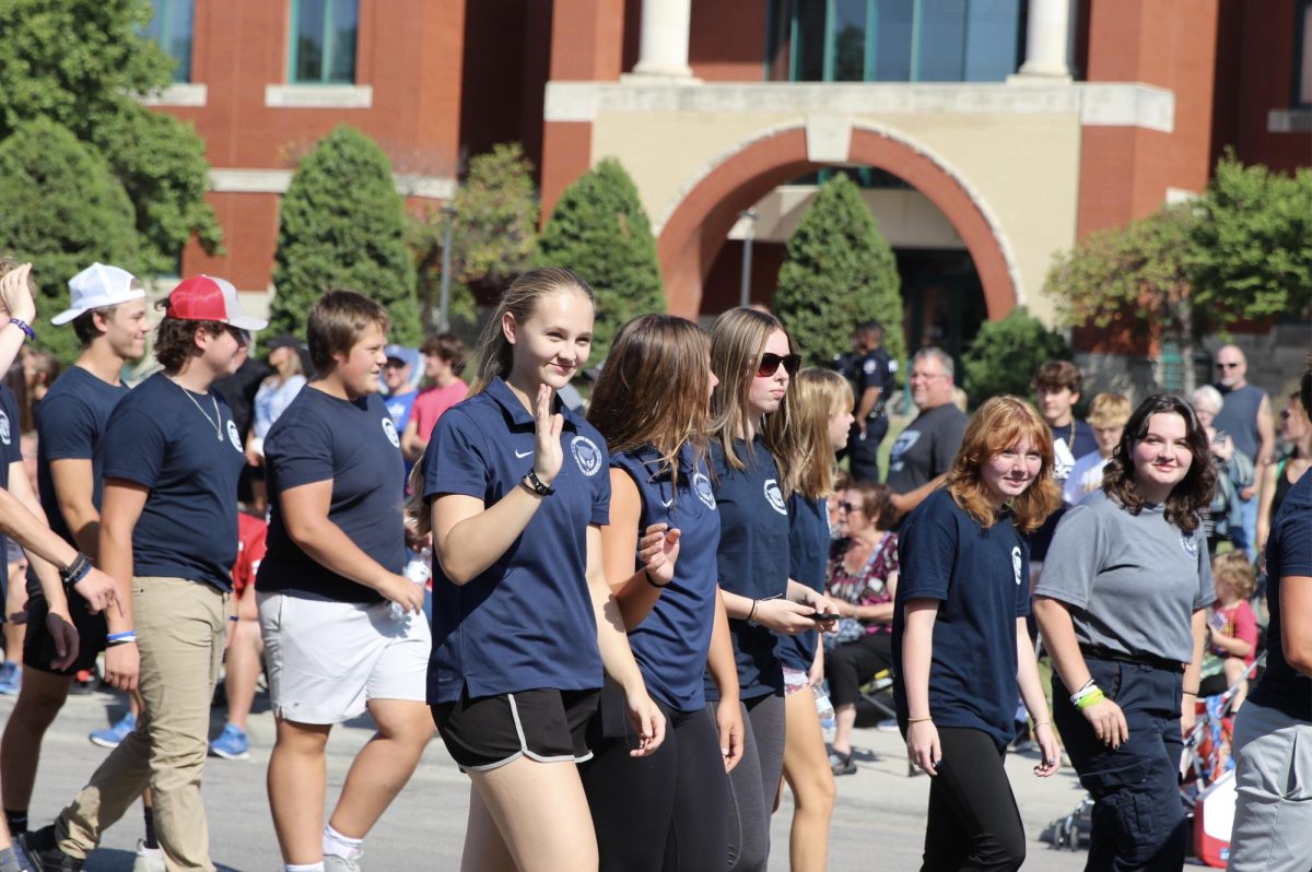 Freshman Elizabeth Price walks in the parade as she smiles and waves towards the crowd.