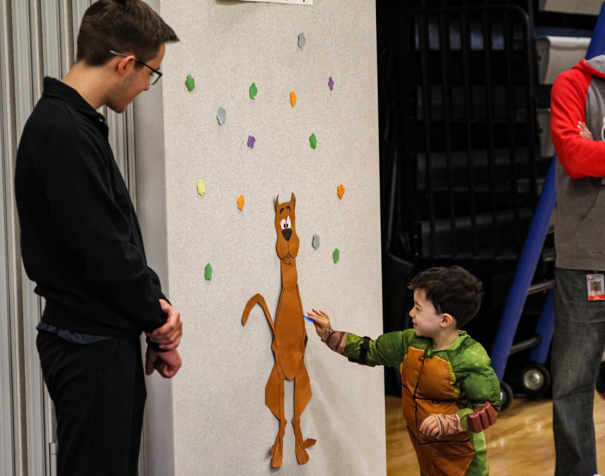 A child participates in an activity provided in the gym by TSA students as Ethan Wolf supervises. 