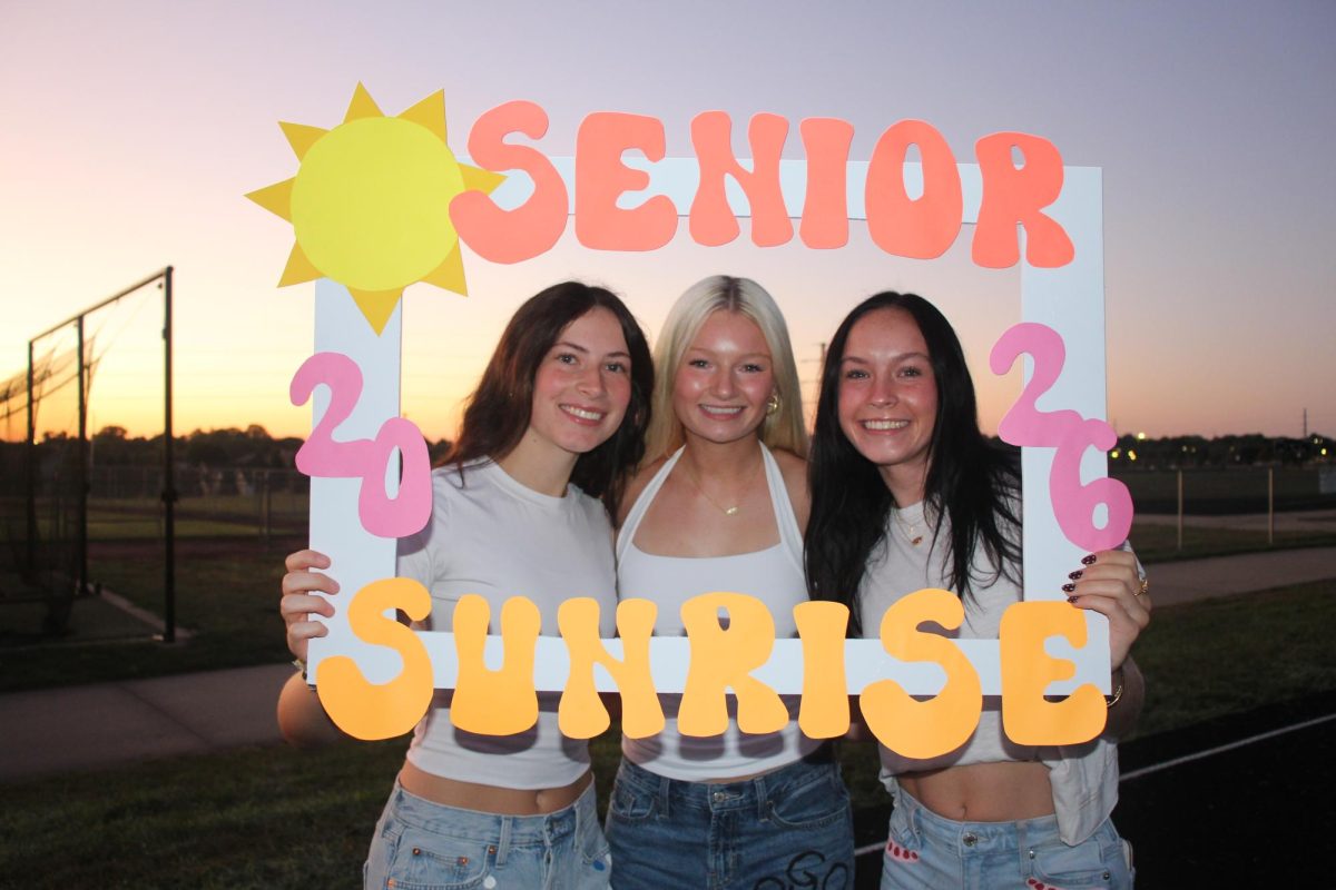 AJ Gaston, Lily Card and Lexi Cooley smiling for the camera with a 'Senior Sunrise' sign.