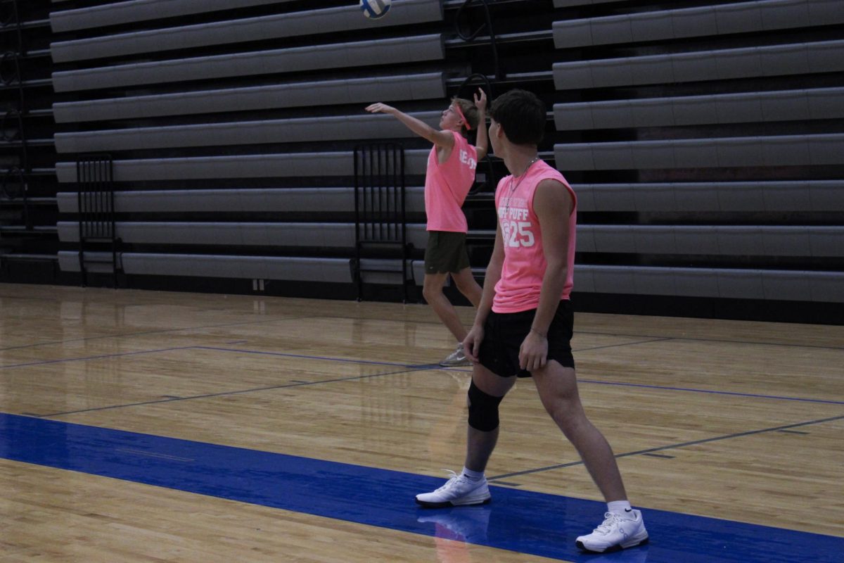Gunnar Cheney serves the ball while Grady England watches.